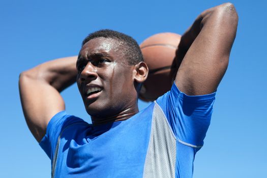 Young basketball player in his early twenties posing with the ball held behind his head.