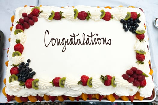 White frosted cake with a fruit border and the message that reads Congratulations.