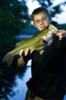 Teenager holds up his catch of a largemouth bass by the spot he was fishing. Shallow depth of field.