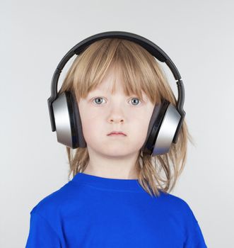 boy with long blond hair listening to music in headphones - isolated on light gray