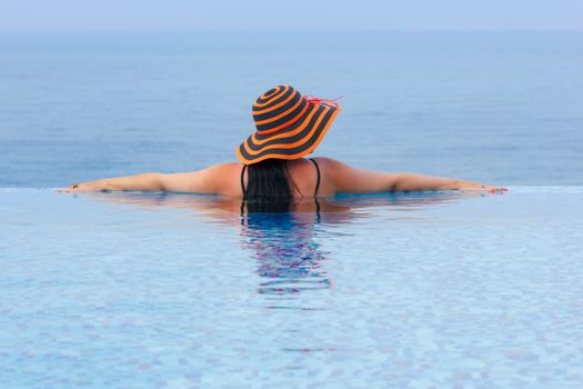 Rear view of young lady enjoying seascape from endless pool. Luxury summer vacation, travel and tourism concept