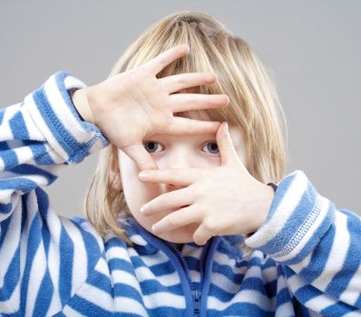 boy with long blond hair looking through a finger frame - isolated on gray