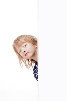 curious boy with long blond hair peeking out from behind a white board looking