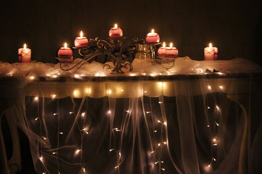 Lit candles on a table draped with netting and fairy lights hanging down. Romantic mood at night time.