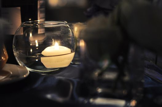 Cream colored, round floating candle, suspended in small glass container. Dark romantic, mood setting.