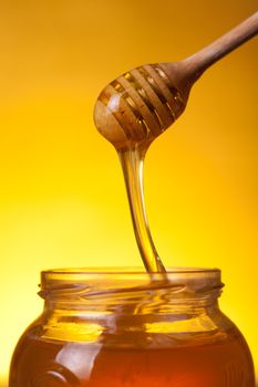 Close-up shot of wooden dipper with flowing honey over yellow background 