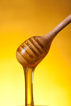 Close-up shot of wooden drizzler with flowing honey over yellow background 