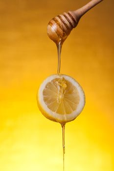 Honey flowing on lemon slice, studio shot over yellow background 