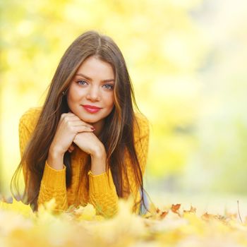 Young cute woman laying on dry leaves in autumn park