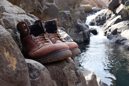 Pair of old hiking boots on rock at river, stream, waterfall at Lotheni. KwaZulu-Natal in the South African Drakensburg mountains