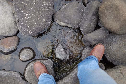 Hiker walking over a river with old boots on rocks at river or stream at Lotheni. KwaZulu-Natal in the South African Drakensburg mountains
