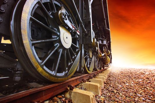 iron wheels of stream engine locomotive train on railways track perspective to golden light forward use for old and classic period land transport and retro vintage style background