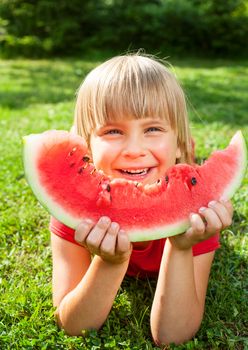 Happy little girl eating watermelon in a garden