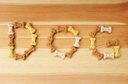 The word DOG spelled out in bone-shaped dog biscuits on a wood background