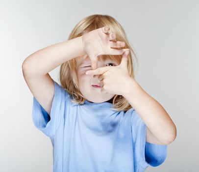 little boy with long blond hair looking through a finger frame - isolated on gray