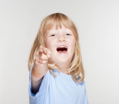 boy with long blond hair pointing towards the camera - isolated on gray