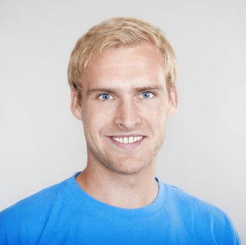 portrait of a young man with blond hair smiling - isolated on light gray