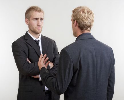 two young businessmen standing, discussing, arguing - isolated on light gray