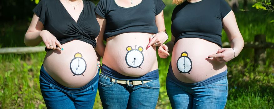 Three pregnant women with clock painted on their bellies