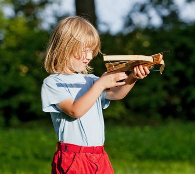 little boy with long blond hair shooting with toy crossbow in the garden