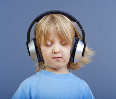 boy with long blond hair listening to music in headphones - isolated on blue