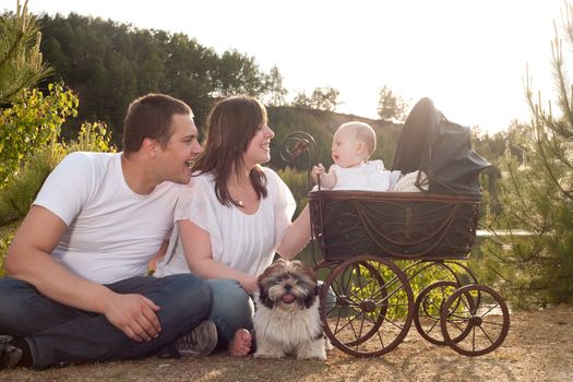 Portrait of parents with their baby girl is sitting in a vintage pram
