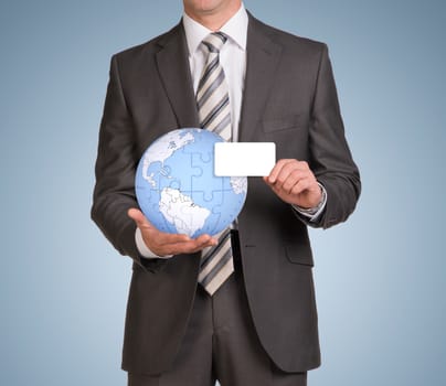 Businessman in suit hold empty card and earth globe consisting of puzzles. Blue background