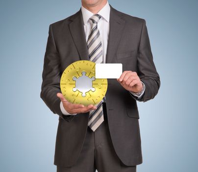 Businessman in suit hold empty card and jigsaw puzzle sphere. Blue background