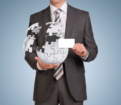Businessman in suit hold empty card and jigsaw puzzle sphere. Blue background