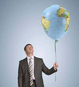 Businessman in suit holding balloon with the image of world map. Blue background