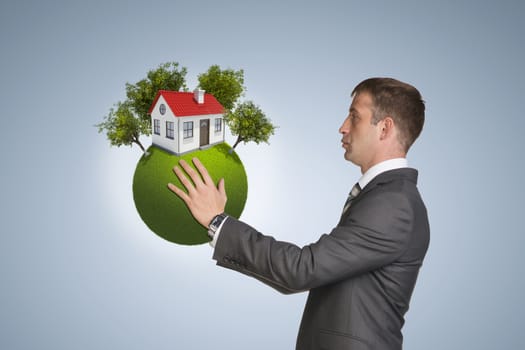 Businessman hold Earth with small house and trees. Blue background