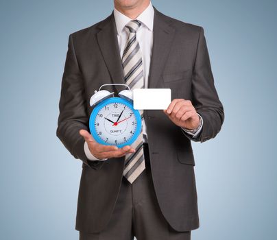 Businessman in suit hold empty card and alarm clock. Blue background