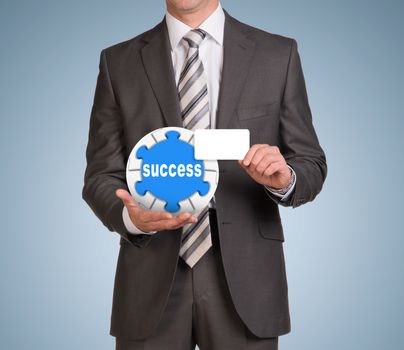 Businessman in suit hold empty card and jigsaw puzzle sphere. Blue background