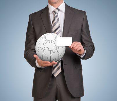 Businessman in suit hold empty card and jigsaw puzzle sphere. Blue background