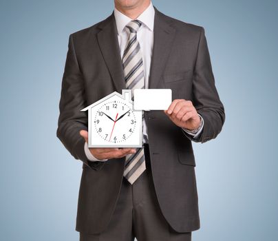 Businessman in suit hold empty card and house icon with clock. Blue background