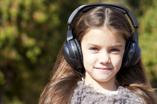 Beautiful little girl listening to music on headphones in autumn park