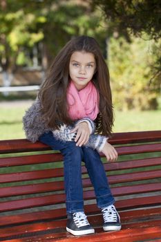 Beautiful little girl sitting on a bench in autumn park