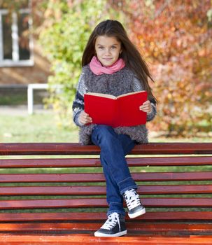 Beautiful little girl sitting on a bench in autumn park