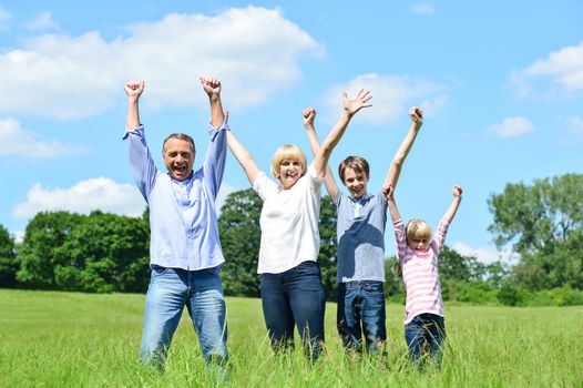 Cheerful family of four lifting arms up in the air