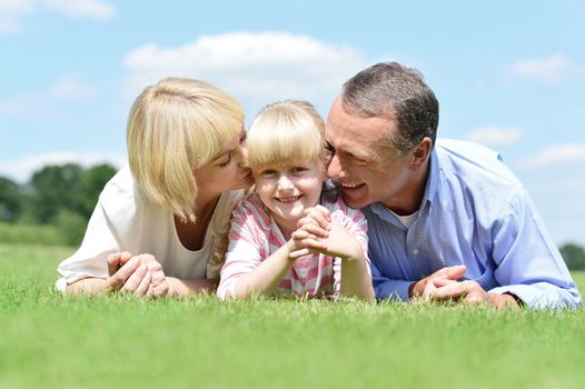 Happy parents lying and kissing their daughter in park