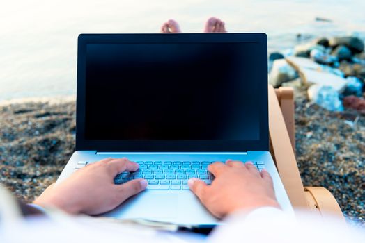 laptop on a man's lap near the sea