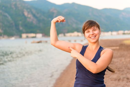 happy girl showing muscles on the beach