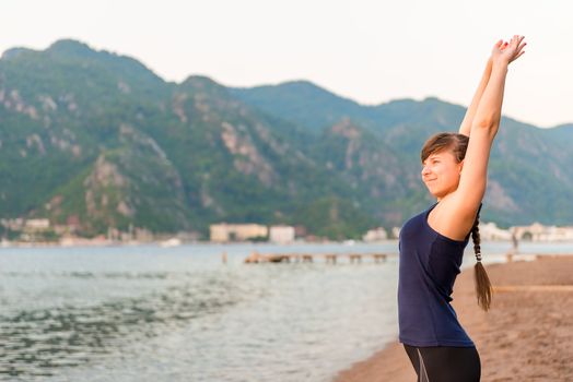 smiling young woman stretches near the sea