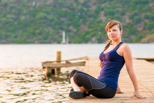 young brunette sitting on a pier in the lotus position