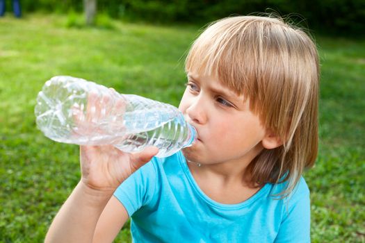 Cute little girl drinking water in a summer garden