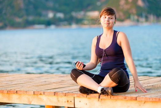 Pensive brunette with the player on the pier at dawn