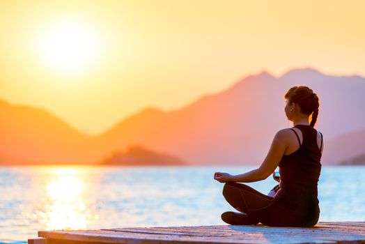 Morning shot of a girl in a lotus position on the pier