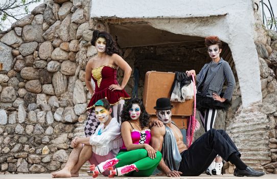 Group of male and female comedia del arte performers sitting on stage