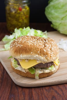 A cheeseburger sitting on a wooden cutting board and surrounded but lettuce, onions, and relish.