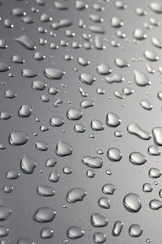 Raindrops on a silver surface with sun shining adding a light effect